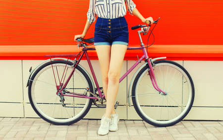 Summer image of legs of beautiful young woman in shorts posing with bicycle in the city on red backgroundの写真素材