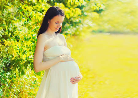 Portrait of happy young pregnant woman walking in sunny summer dayの写真素材