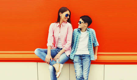 Portrait of mother with son teenager in sunglasses, checkered shirts on an orange backgroundの写真素材
