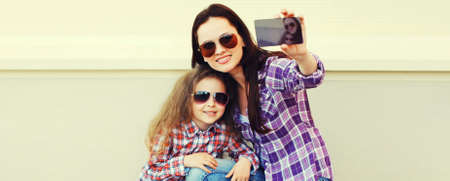 Portrait of happy smiling mother and child taking selfie by smartphone together in the city