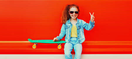 Portrait of cheerful laughing little girl child posing with skateboard in the city on colorful...