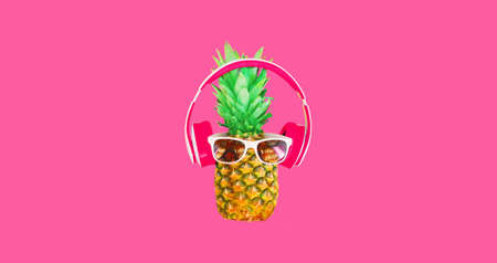 Close up of funny pineapple listening to music in headphones on pink backgroundの写真素材