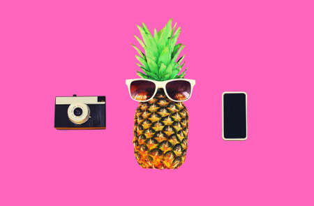 Fashion pineapple with sunglasses, film camera, blank black screen smartphone on colorful pink backgroundの写真素材