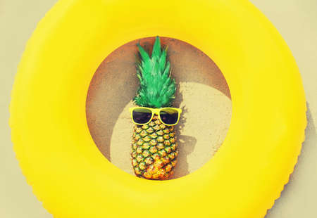 Summer vacation concept - pineapple and yellow inflatable ring on beach sand backgroundの写真素材