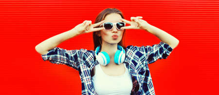 Portrait of stylish young woman with headphones listening to music blowing her lips sends air kiss...