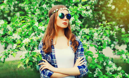 Portrait of beautiful young woman wearing floral headband, sunglasses in garden or parkの写真素材