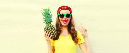Summer portrait of happy smiling woman with pineapple wearing sunglasses, red baseball cap on white backgroundの写真素材