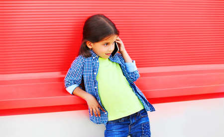Portrait of little girl child calling on smartphone looking away in the city on pink backgroundの写真素材