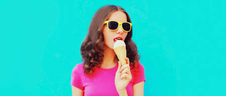 Portrait of happy young woman eating ice cream wearing summer sunglasses on blue background