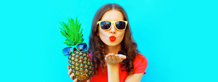 Summer portrait of happy young woman with pineapple blowing her lips with red lipstick wearing...