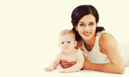 Portrait of happy smiling mother and baby lying on the floor together on white background
