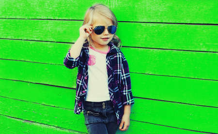 Portrait of stylish little girl child model posing on vivid green background