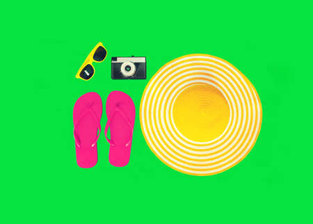 Summer vacation, yellow straw beach hat with pink flip flops, film camera and sunglasses on colorful green background, top viewの写真素材