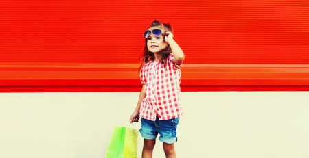 Little girl child with shopping bags in the city on red backgroundの写真素材