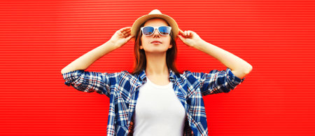 Portrait of young woman wearing summer straw hat, shirt on red background, blank copy space for...