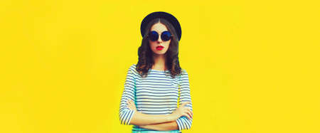 Portrait of stylish young woman model posing wearing striped t-shirt and summer straw round hat on yellow background, blank copy space for advertising textの写真素材