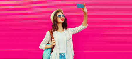 Portrait of happy smiling young woman taking selfie with smartphone wearing summer straw hat,...