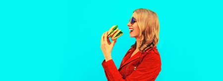 Portrait of stylish happy smiling young woman with tasty big burger fast food on blue background,...