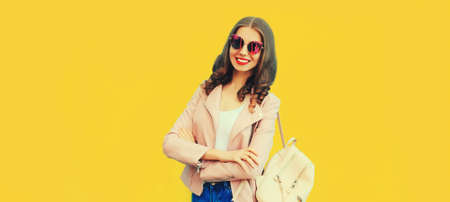 Portrait of beautiful smiling young woman wearing backpack on yellow background, blank copy space for advertising textの写真素材