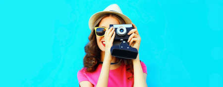 Summer portrait of young woman photographer with film camera on blue background