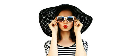 Portrait of beautiful young woman blowing her lips with red lipstick sending sweet air kiss wearing black summer straw hat isolated on white backgroundの写真素材