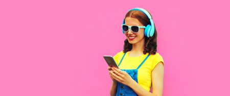Portrait of smiling young woman in headphones listening to music with smartphone on pink background, blank copy space for advertising textの写真素材
