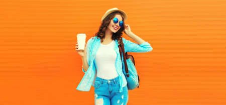 Summer portrait of happy smiling young woman with cup of coffee wearing straw hat, backpack and...