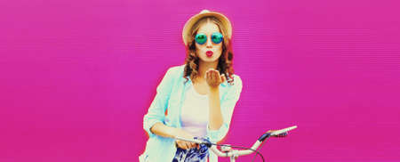 Summer colorful image of happy young woman blowing her lips with bicycle on vivid pink background