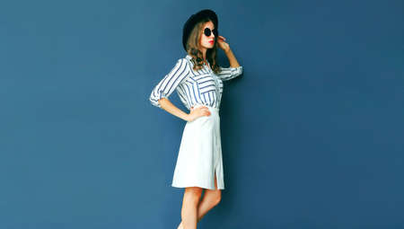 Portrait of beautiful young woman wearing white striped shirt, black round hat on dark blue backgroundの写真素材