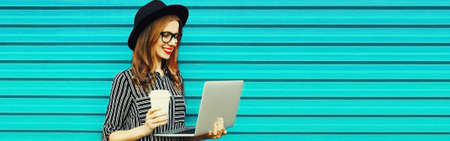 Portrait of modern happy smiling young woman working with laptop on blue background, blank copy space for advertising textの写真素材