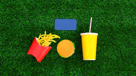 Fast food concept - blank screen smartphone, burger, french fries and cup of juice on the grass backgroundの写真素材