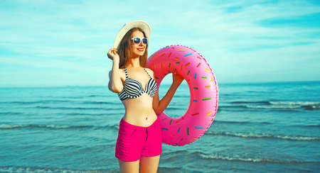 Portrait of happy smiling young woman with inflatable ring wearing straw hat on beach on sea backgroundの写真素材