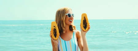 Summer portrait of happy smiling young woman with papaya on the beach on sea backgroundの写真素材