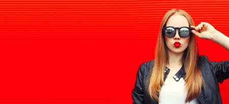 Portrait of blonde young woman blowing her lips with lipstick sending air kiss wearing sunglasses on...