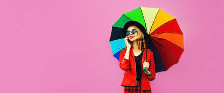 Portrait of happy smiling woman calling on smartphone with colorful umbrella wearing jacket on pink background, blank copy space for advertising textの写真素材