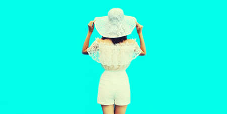 Beautiful woman model wearing summer straw white hat on blue background, rear viewの写真素材