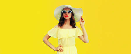 Portrait of beautiful woman model wearing summer straw white hat on yellow backgroundの写真素材