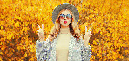 Autumn portrait stylish woman model wearing coat, round hat posing on yellow leaves background