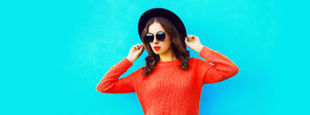 Portrait of beautiful young woman wearing black round hat, sweater on blue backgroundの写真素材