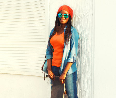 Portrait of happy smiling young african woman with skateboard wearing pink hat in the cityの写真素材