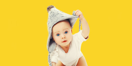 Portrait of cute little baby wearing gray knitted hat on yellow backgroundの写真素材