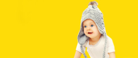 Portrait of cute little baby wearing gray knitted hat on yellow background