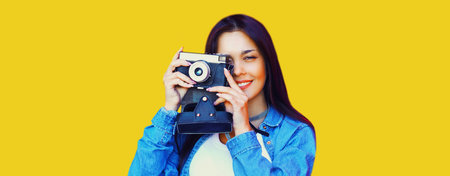 Portrait of young woman photographer with vintage film camera on yellow backgroundの写真素材