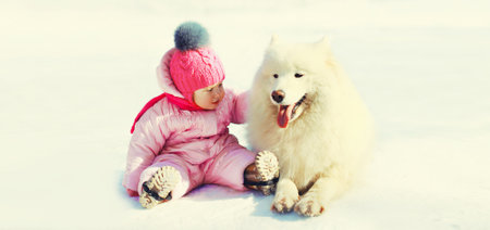 Happy little child playing with white Samoyed dog in winter park