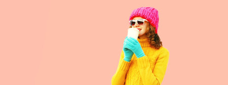 Winter portrait of young woman drinking hot coffee looking away wearing colorful knitted sweater,...
