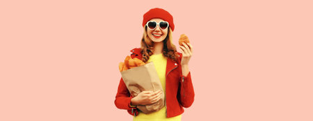 Portrait of happy smiling young woman holding grocery shopping paper bag with long white bread baguette wearing red french beret, heart shaped sunglasses on pink backgroundの写真素材