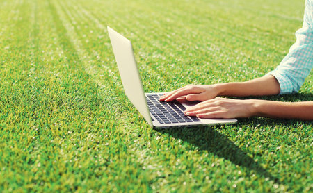 Female hands woman working with laptop in the park on green grass backgroundの写真素材