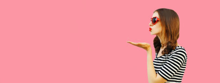 Portrait of beautiful young woman blowing her lips with lipstick sending sweet air kiss wearing red...