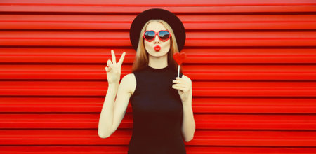 Portrait of beautiful young woman with lollipop blowing her lips with lipstick sending sweet air...