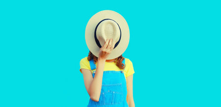Portrait of unknown stranger young woman covering her face with summer straw round hat on blue...
